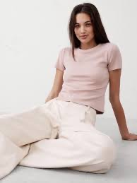 A girl sitting down with a pink t-shirt on and white pants.