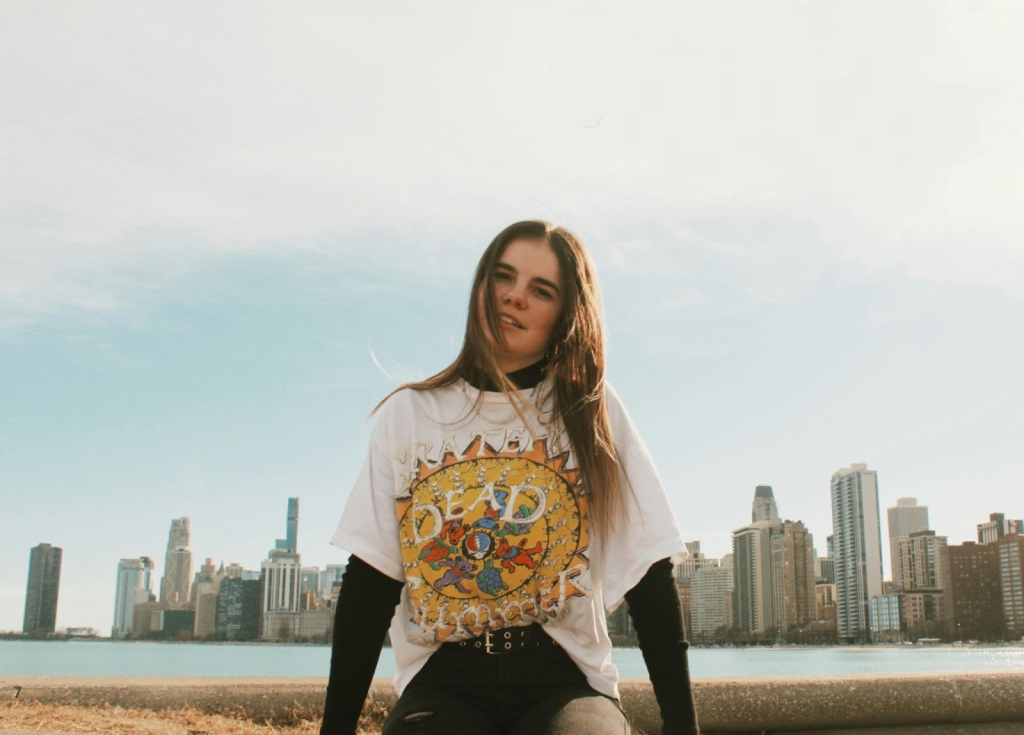 A girl wearing a graphic tee with a long sleeve shirt under neath with a city scape in the back ground.
