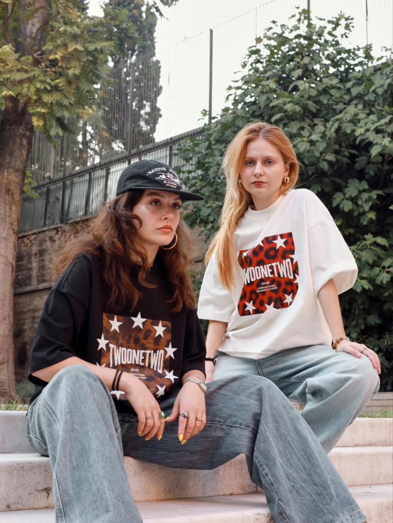   Two girls sitting on stares wearing graphic tee shirts and jeans