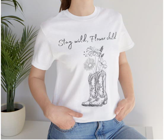 A picture of a shirt that says stay wild flower child with boots and flowers on it.