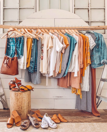 bright colored clothes on a rack. with 7 pairs of shoes underneath it.