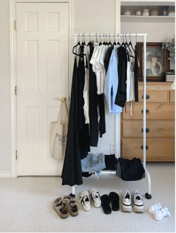 A clothes rack with clothes on it. with shoes below it