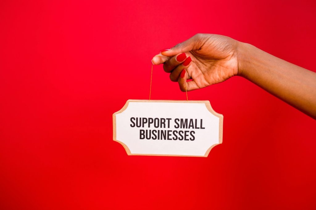A hand holding a sign that says support small businesses.